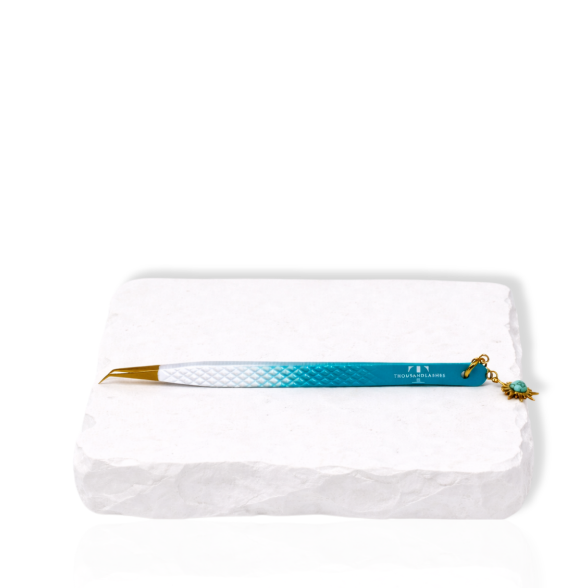 Blue gradient angled eyelash extension tweezer with decorative charm displayed on a white stone surface.