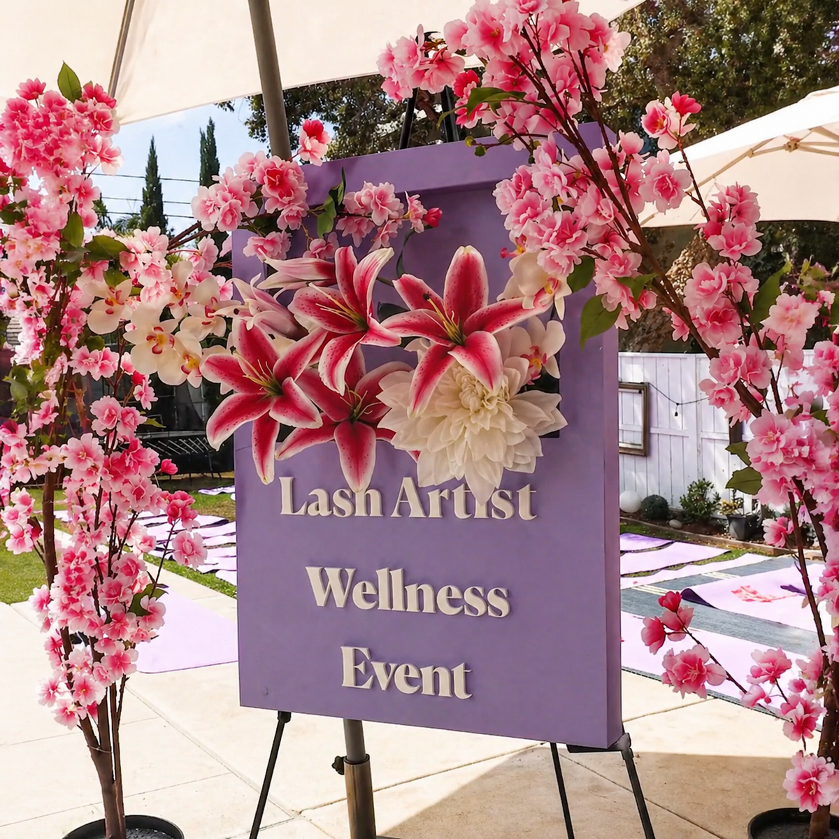 Floral photo backdrop with a sign for a lash artist wellness event.
