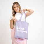 Lash artist carrying Local Lash Plug purple tote bag over shoulder, showing a convenient bag for lash studio essentials