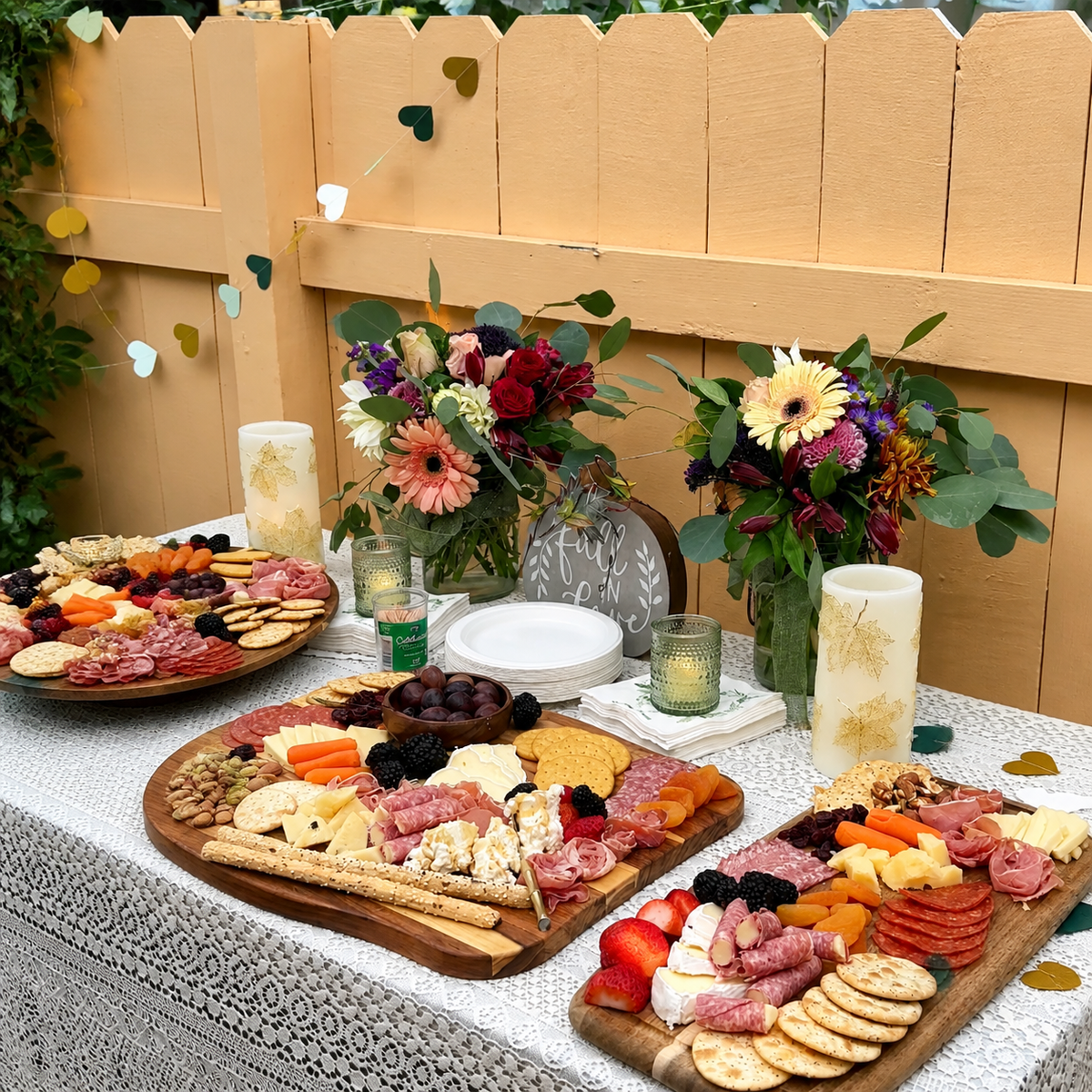 Outdoor brunch setup with a charcuterie board, fruits, cheese, and floral decorations.