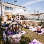 Outdoor wellness event setup with yoga mats, seating areas, and attendees gathering.