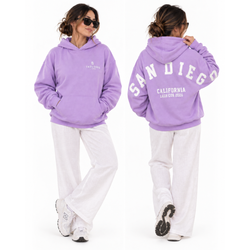 Person wearing a lavender oversized Thousand Lashes hoodie showing the front logo and back San Diego California Lash Con 2026 design.