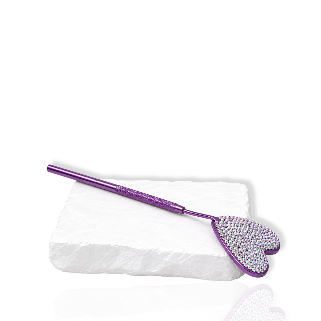 Purple eyelash extension mirror with a rhinestone heart-shaped head displayed on a white stone surface.