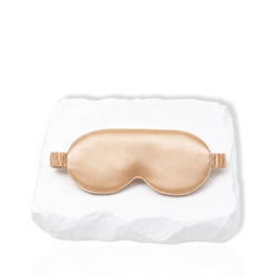Silk lash mask with padded eye-shaped design and adjustable strap displayed on a white stone surface.