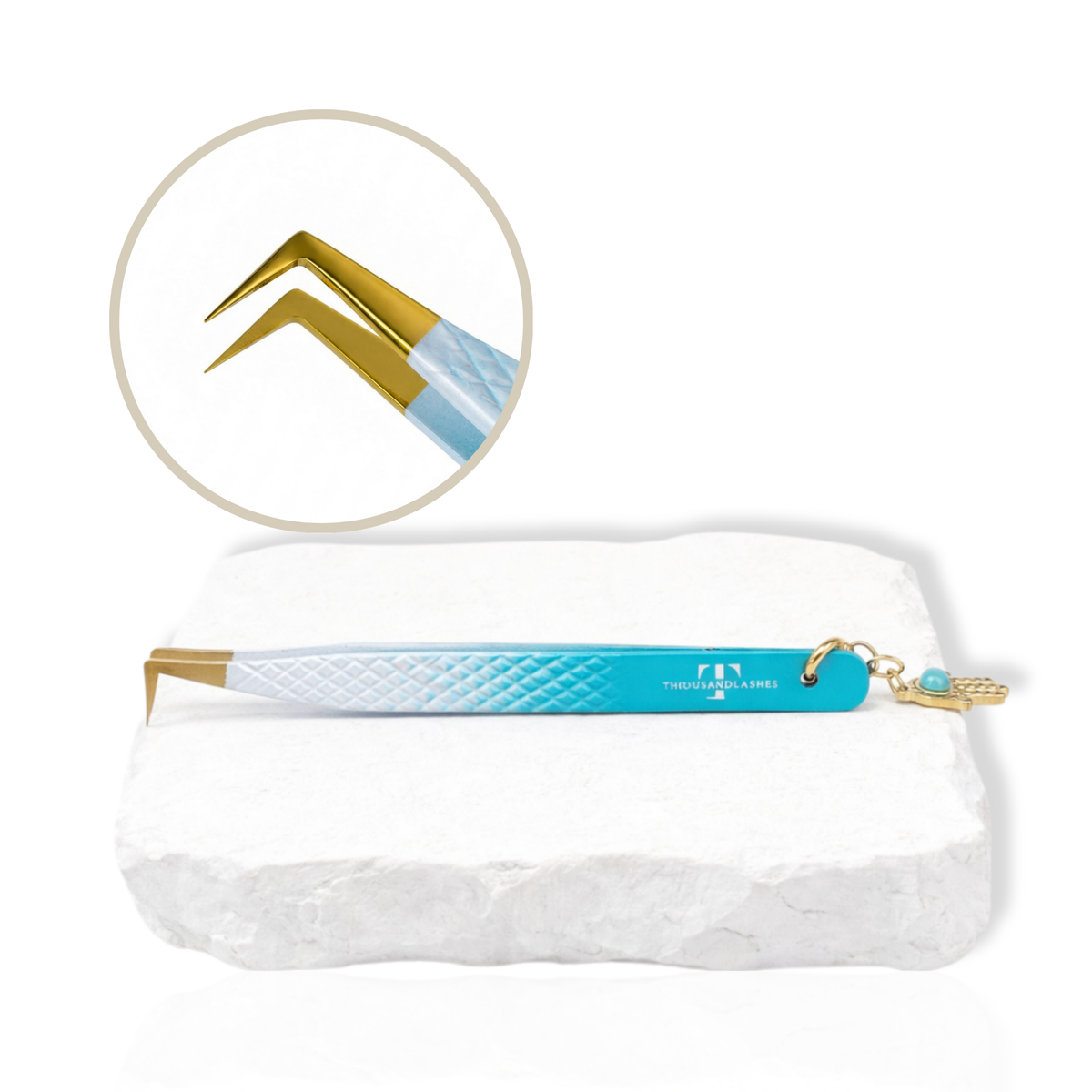 Thousandlashes Evil Eye angled lash tweezer with gold tip and Hamsa charm on a white stone surface.