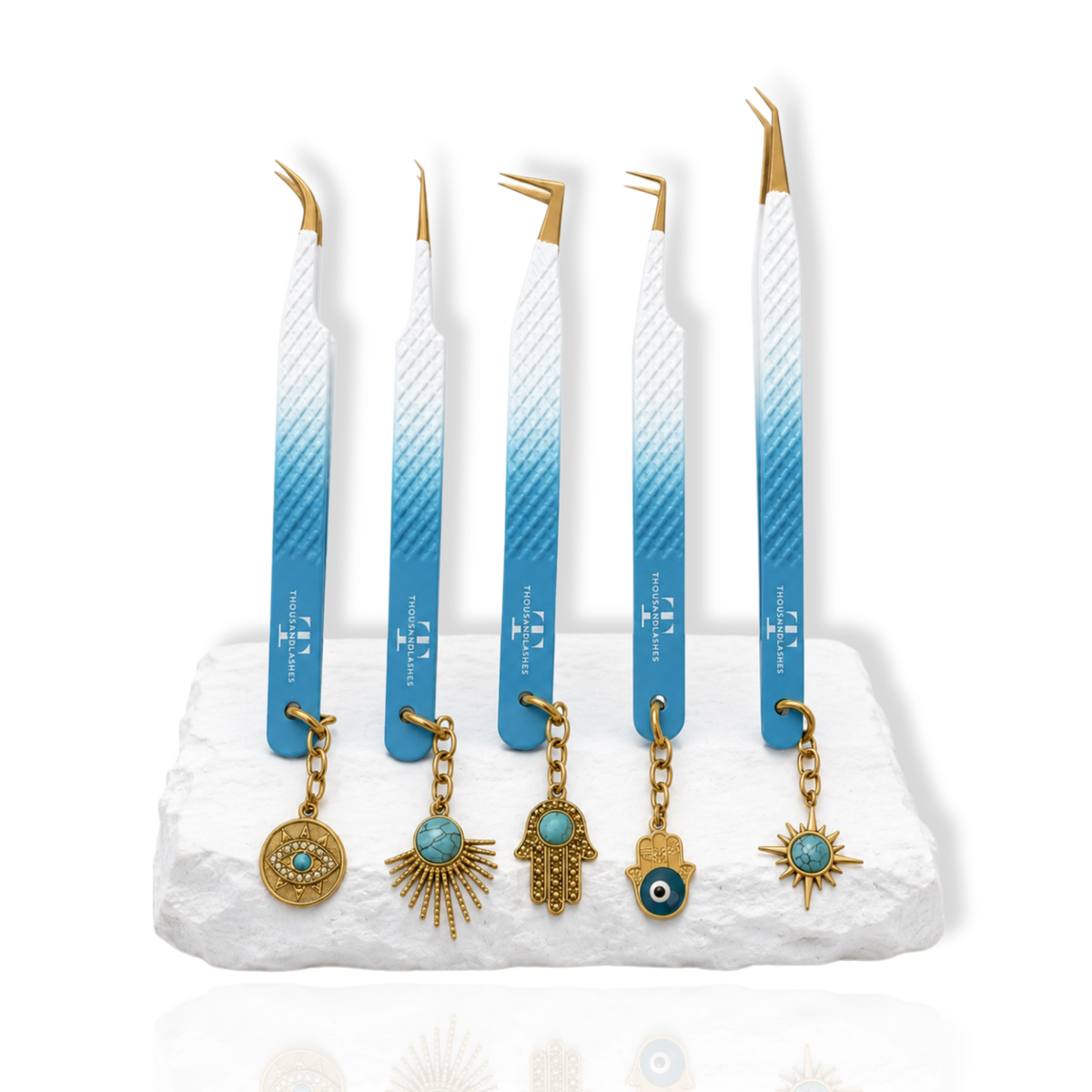 Thousandlashes Evil Eye tweezer set with five blue-and-white lash tweezers, gold tips, and decorative charms on a white stone surface.