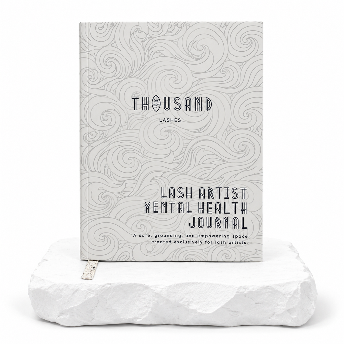 Thousandlashes Lash Artist Mental Health Journal with a gray wave-pattern cover displayed on a white stone surface.
