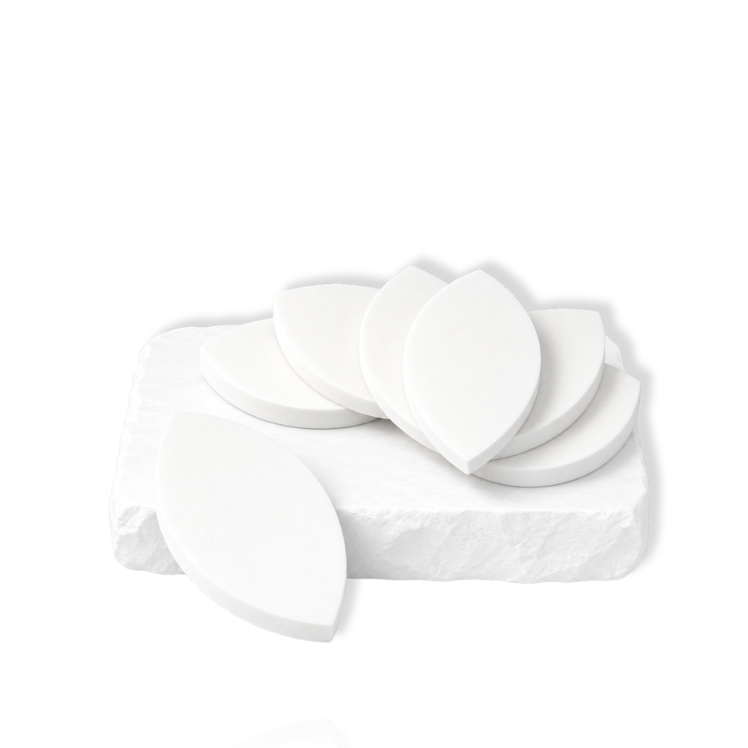 White leaf-shaped makeup sponges stacked and arranged on a white stone slab.