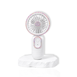 White portable lash fan with rhinestone detailing displayed on a white stone surface.