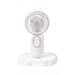 White portable lash fan with rhinestone detailing displayed on a white stone surface.