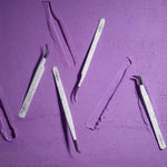 Eyelash extension tweezer set with multiple white marble-pattern tweezers displayed on a purple background.