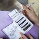 Lash artist holding a lash tweezer beside an eyelash extension tray during a lash appointment