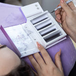 Lash artist preparing eyelash extensions with a tweezer and lash tray during a lash appointment