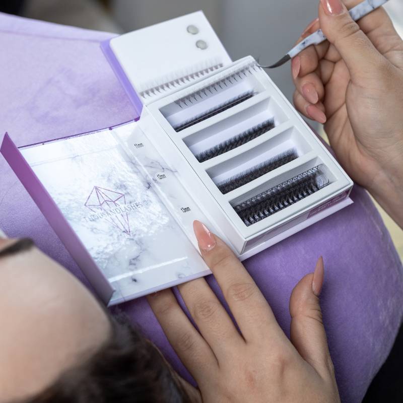 Lash artist preparing eyelash extensions with a tweezer and lash tray during a lash appointment