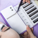 Lash artist using a Thousandlashes Noir Collection curved tweezer to pick up lash extensions from a tray.