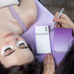 Lash artist using a curved tweezer to work on eyelash extensions with a client resting on a lash bed and wearing under-eye gel pads.
