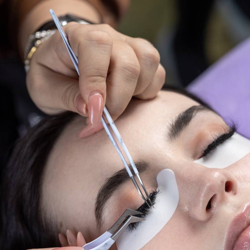 Lash artist using curved tweezer during eyelash extension application on a client