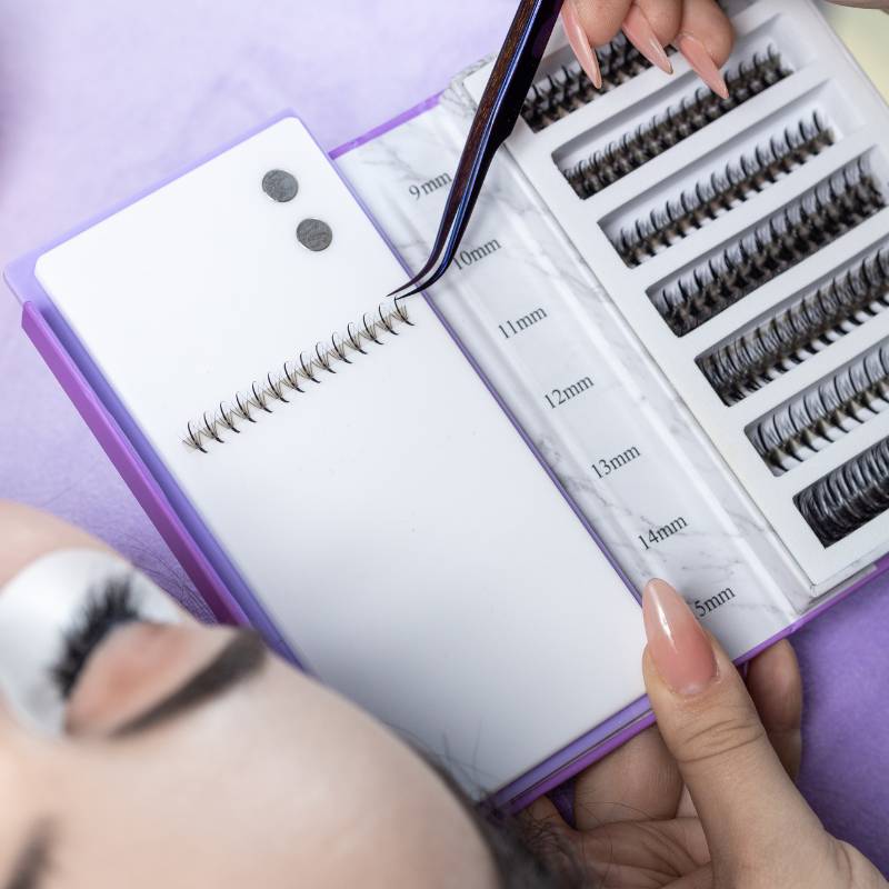 Noir Collection lash tweezers displayed on white platforms against a purple background.