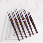 Set of purple professional eyelash extension tweezers arranged on a white marble surface for lash application and precision beauty tools.